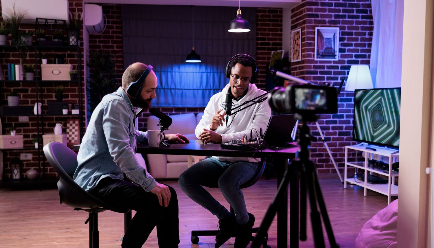 Two people recording a podcast in a studio with brick walls and professional equipment.