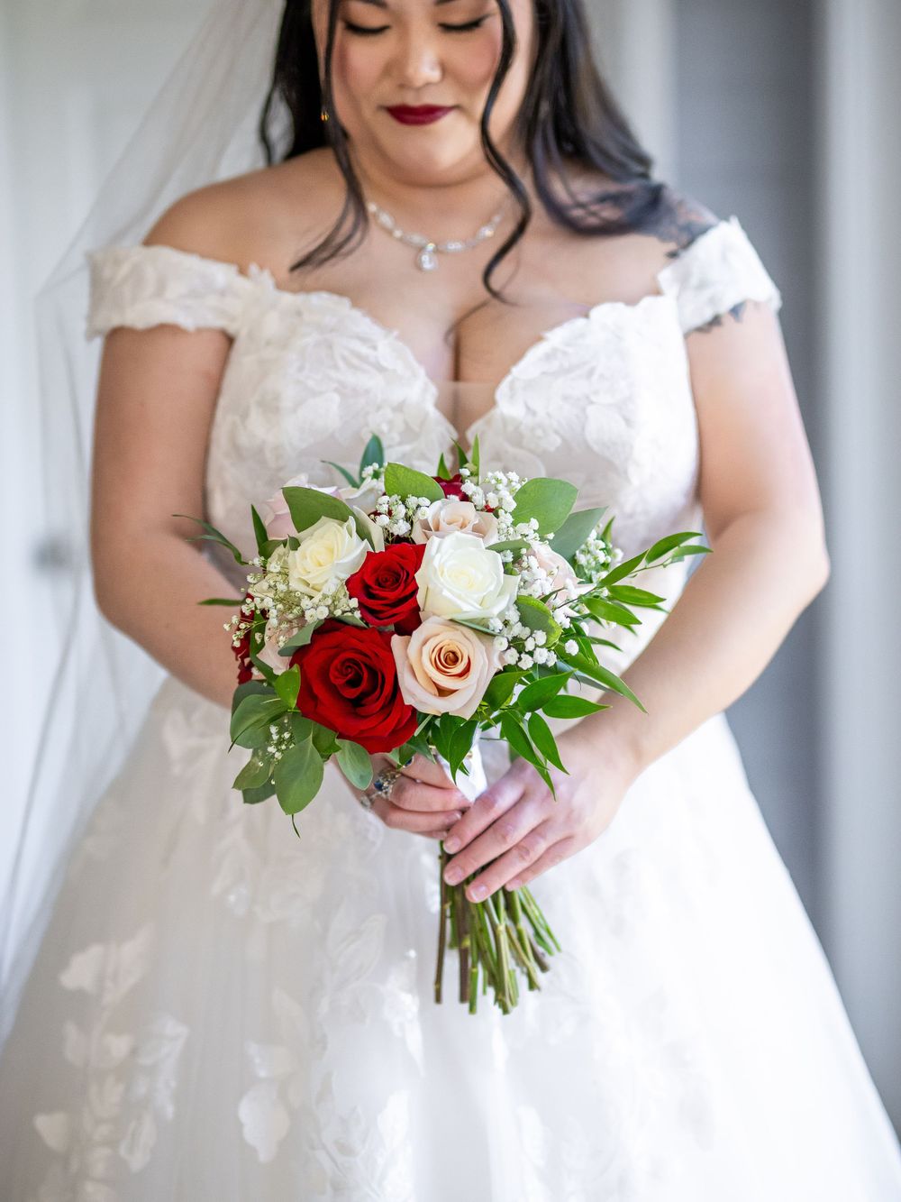 Close-up of a bridal bouquet featuring red and white roses with greenery against a white wedding dress.