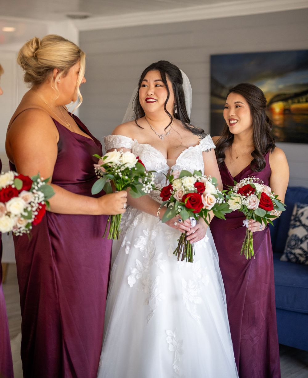 A bridal party in burgundy dresses holds matching bouquets while sharing a joyful moment.
