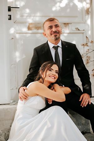 A joyful couple poses together outdoors, with the bride in white and groom in black suit.