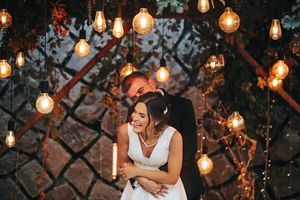 A romantic couple embraces under glowing string lights at their wedding celebration.