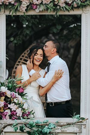 A happy couple shares a candid moment in front of a floral arch during their wedding celebration.