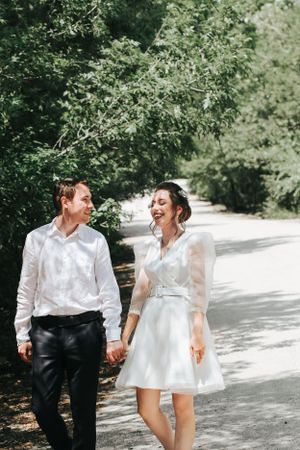 Candid moment of laughter between newlyweds walking on a tree-lined path.
