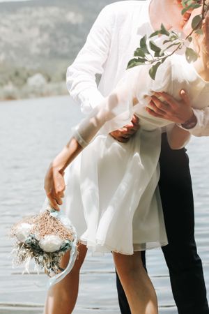 Artistic wedding photo showing couple with bridal bouquet by waterfront.