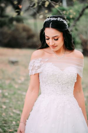 Bride in off-shoulder lace wedding gown with delicate crown looks down gracefully.