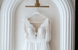White wedding dress hanging in an arched alcove displaying intricate bodice details.
