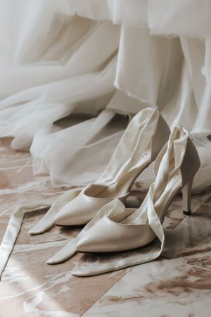 Elegant white high-heeled wedding shoes photographed on marble flooring.