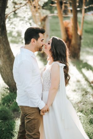Romantic wedding couple shares an intimate moment in a sunlit forest setting.