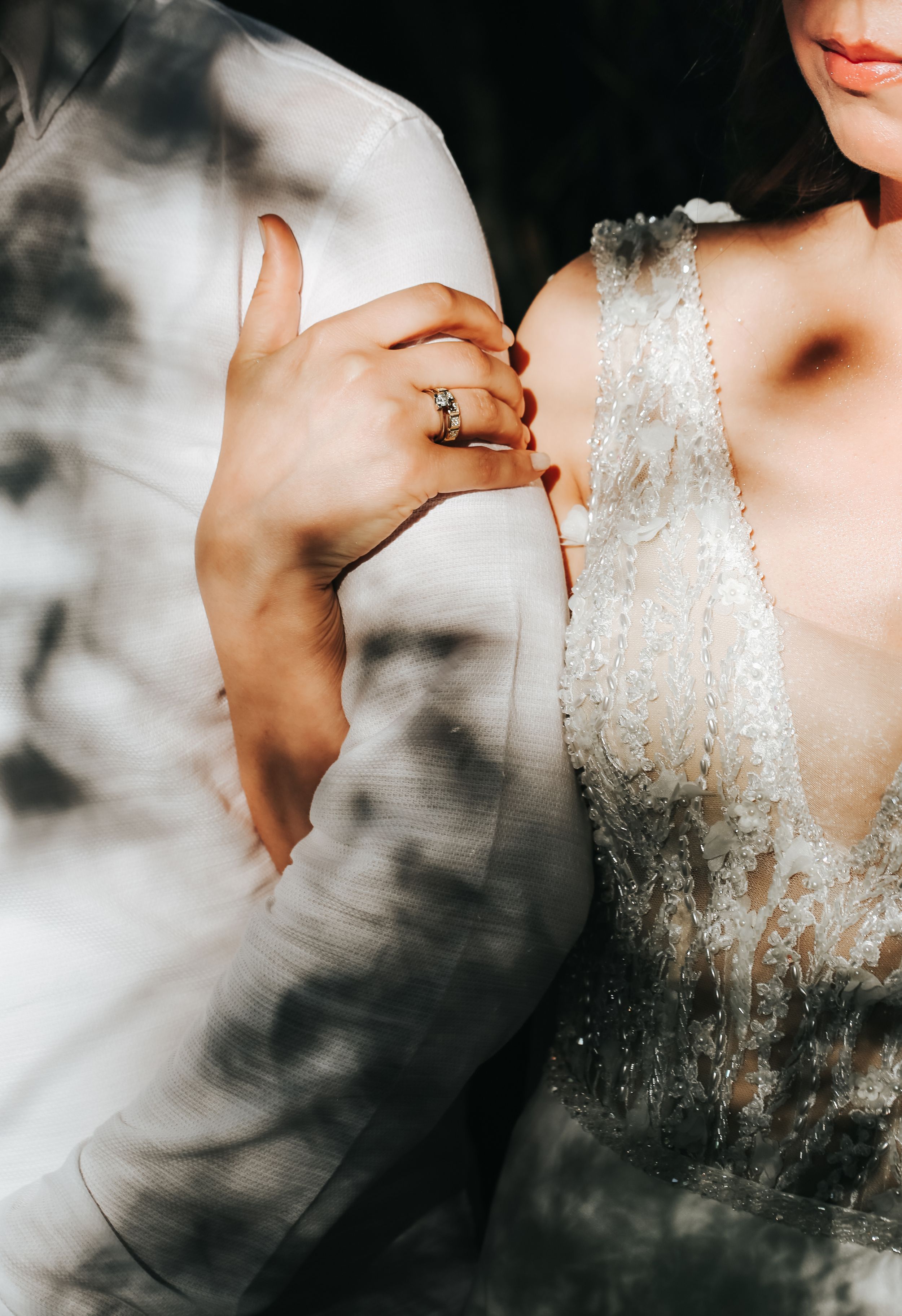 Close-up detail of intricate lace wedding dress and hands against a dreamy background with shadows.
