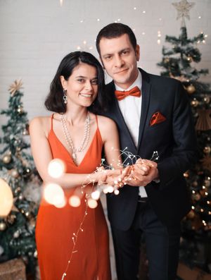 A couple in festive attire poses with sparklers in front of a Christmas tree.