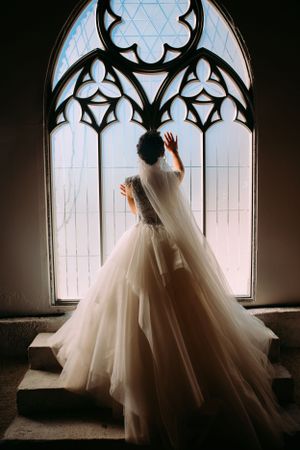 A flowing white wedding gown silhouetted against a Gothic church window with ornate tracery.