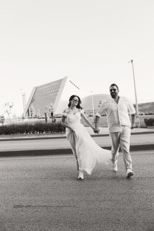 Black and white photo of newlyweds walking together in front of modern architecture.