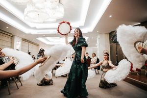 A dancer in an emerald green dress performs with a tambourine while others wave white feather fans in an elegant venue.