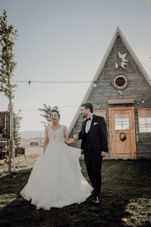 Wedding couple posing in front of rustic A-frame chapel with wooden details.