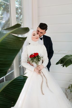 Modern wedding portrait with couple by white wall and tropical leaves.