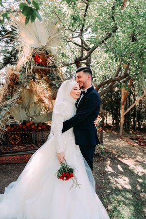 Newlyweds share intimate moment under blooming trees with bohemian decor.