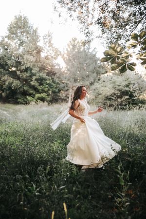 A bride in a flowing white dress twirls joyfully in a sunlit meadow during a romantic outdoor photoshoot.