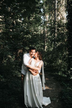 Romantic candid shot of couple embracing on forest path in casual wedding attire.