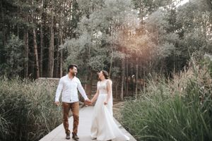 Couple walking hand in hand on pathway through lush green forest setting.