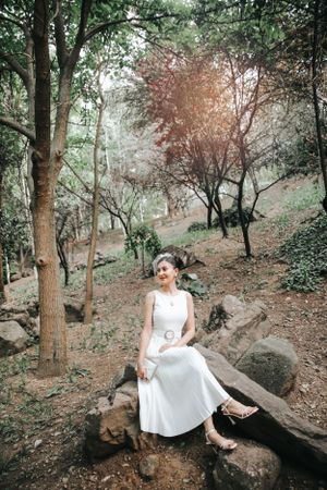 Wedding portrait in a forest setting with rustic rocks and dappled sunlight.