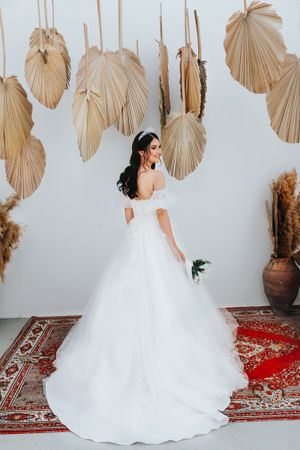 Elegant wedding dress displayed against a backdrop of dried palm fronds and a red oriental rug.