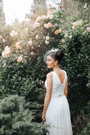 Elegant white wedding dress photographed against blooming rose bushes in a garden.