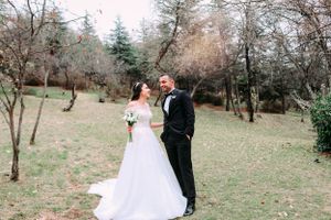 A wedding couple poses together in a natural outdoor setting with bare winter trees.