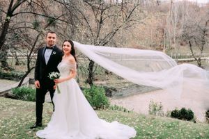 A wedding couple poses outdoors as the bride's long veil flows dramatically in the wind.