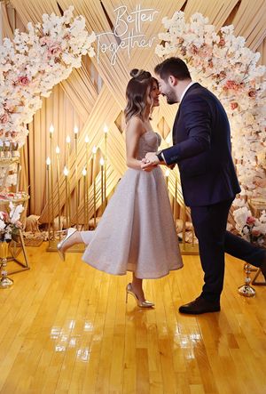 Wedding couple posing under floral arch with gold backdrop and mood lighting.