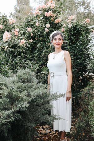 White midi dress styled with vintage accessories against a backdrop of blooming roses.