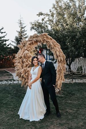 Newlyweds pose under rustic dried pampas grass arch during outdoor wedding celebration.