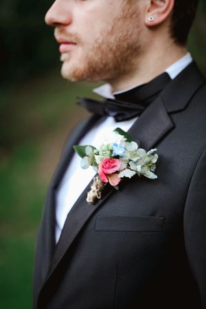 Close-up of delicate pink and white floral boutonniere on black tuxedo lapel.