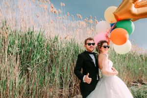 Wedding couple posing with colorful balloons against tall reeds in natural setting.