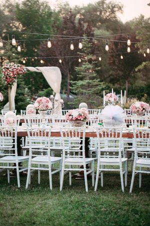 Outdoor wedding reception setup with white chiavari chairs and hanging string lights.