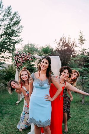 Group of women in colorful dresses posing playfully outdoors at a wedding.