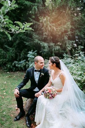 Wedding couple sitting intimately on rustic wooden steps surrounded by lush garden greenery.