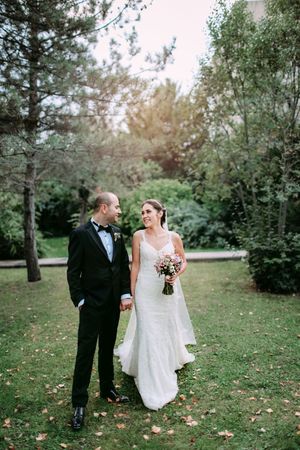 A romantic wedding photo of a couple standing together on a lawn surrounded by trees at sunset.