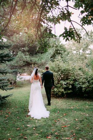 Wedding couple walking hand in hand through a lush garden pathway.