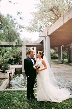 Wedding couple standing by a modern architectural structure with water features and greenery.