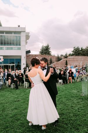 First dance at outdoor wedding with guests watching from white chairs.
