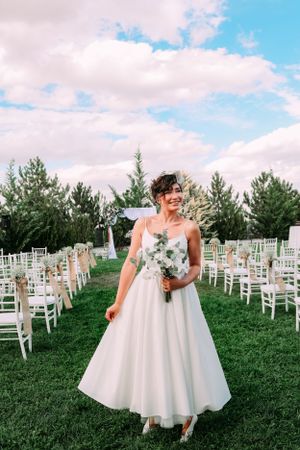 A wedding setup outdoors with white chairs arranged on a lawn surrounded by evergreen trees.