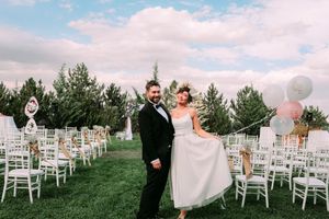 Wedding couple poses in outdoor ceremony setup with white chairs and balloons.