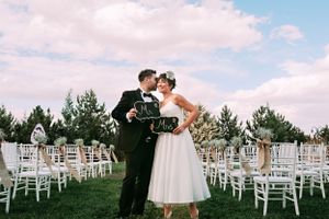 An outdoor wedding moment with white chairs arranged on green grass under blue skies.