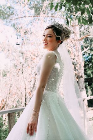 Bride in sparkly ball gown and tiara poses against blooming cherry blossom trees.