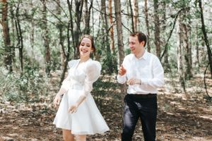 Joyful couple running through a forest setting in wedding attire.