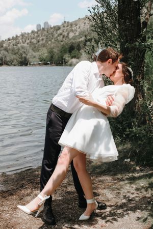 Romantic wedding couple sharing an intimate moment by a lake with mountains in the background.