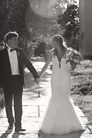 Black and white photo of couple walking hand in hand on garden path in wedding attire.