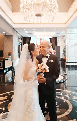 A wedding couple shares a tender moment under an ornate chandelier in an elegant venue.