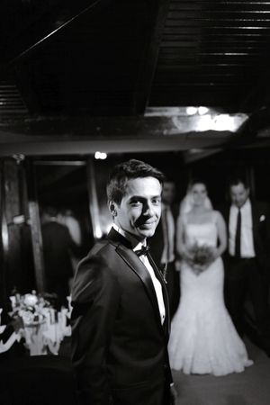 A black and white wedding photo features a groom in a tuxedo with wedding guests in background.