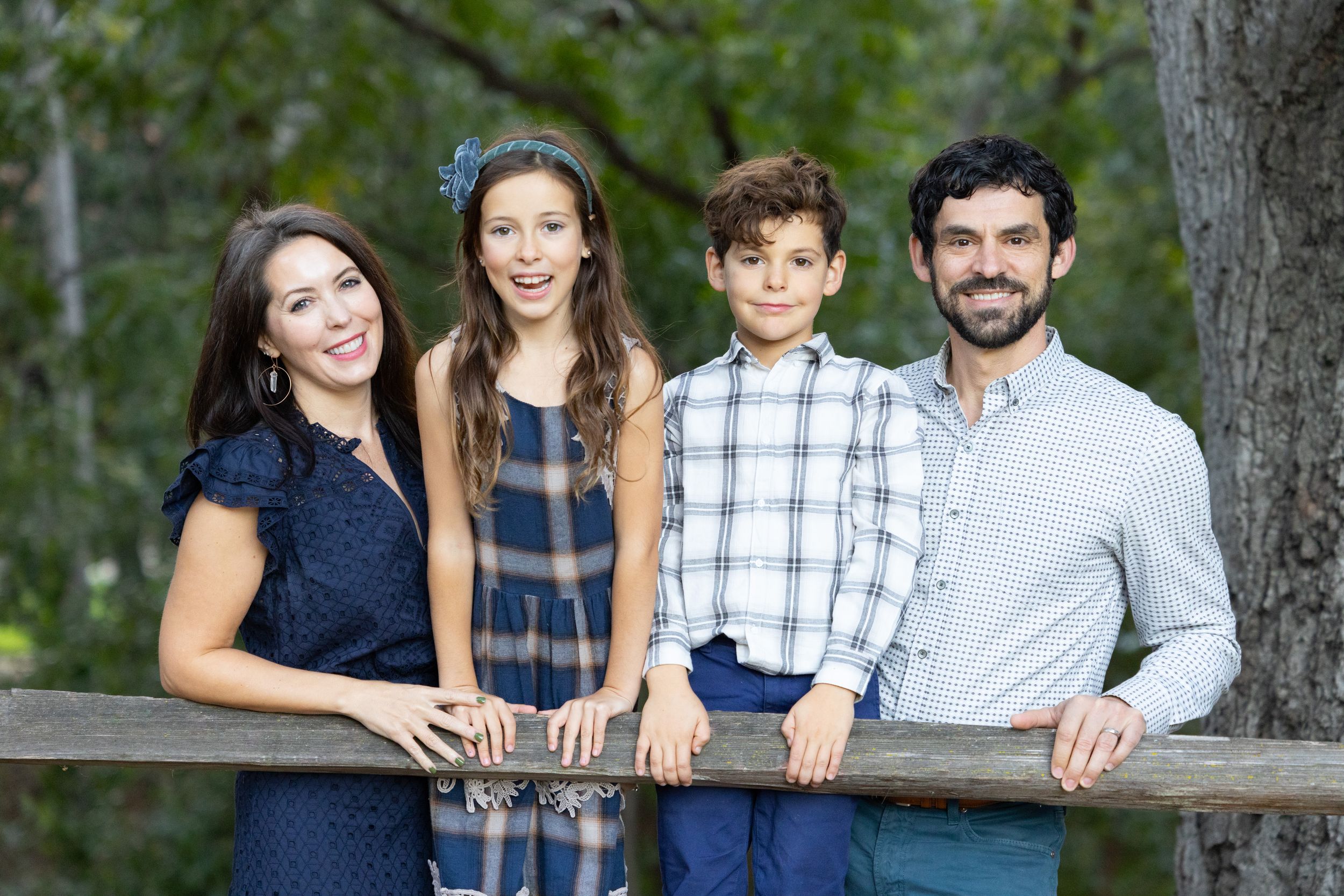 A family of 4 poses at a wooden fence